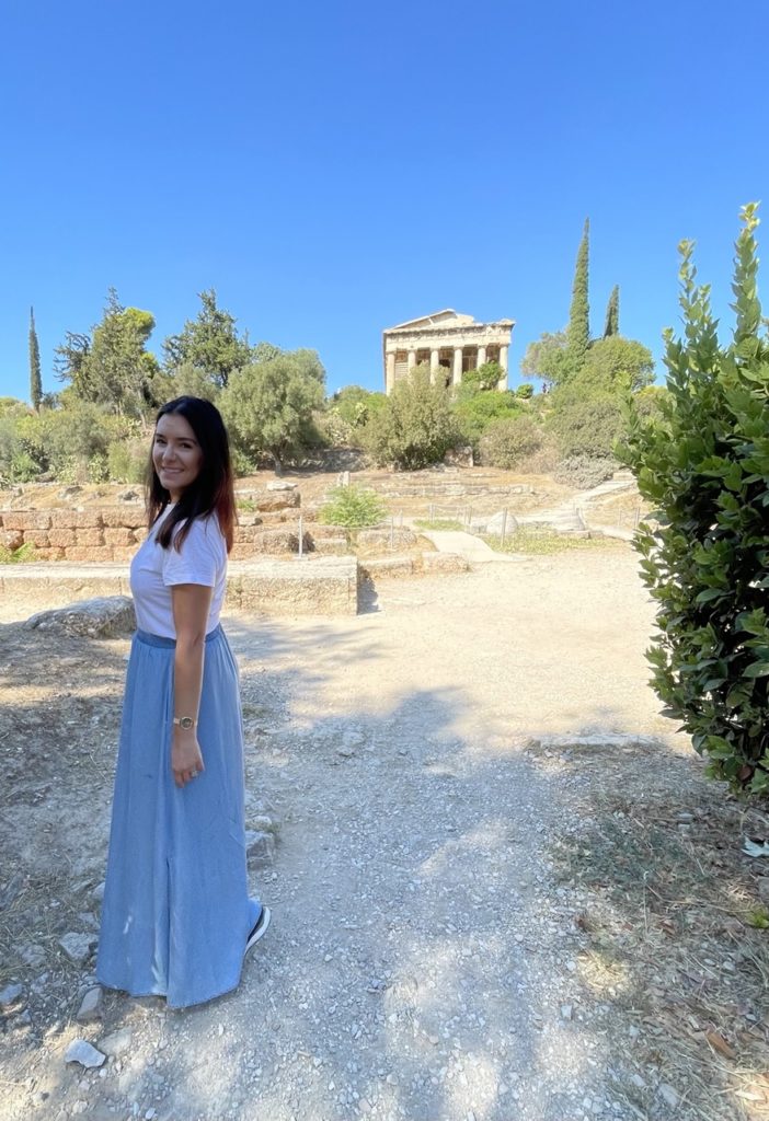 Girl in Greece wearing a blue skirt and white shirt smiling. 