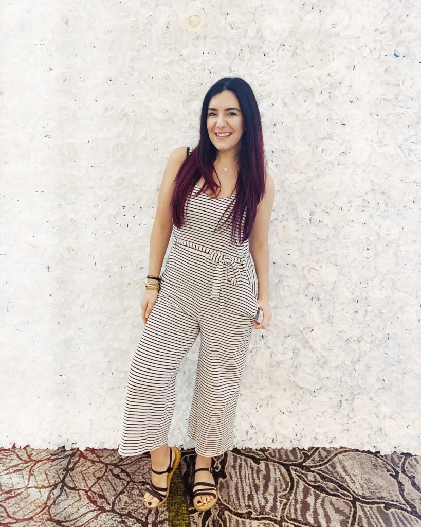Girl in a jump suit standing against and wall smiling